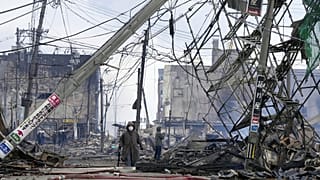  أشخاص يسيرون في السوق المتضررة التي أحرقتها النيران بعد الزلزال الذي ضرب واجيما، محافظة إيشيكاوا، اليابان، 2 يناير 2024.