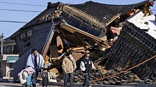 Un uomo porta le sue cose davanti a una casa crollata in seguito a un terremoto a Wajima, nella prefettura di Ishikawa, in Giappone, martedì 2 gennaio 2024\.