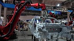 FILE - Visitors look at the robotic arms assembly a vehicle frame during the annual World Robot Conference at the Etrong International Exhibition and Convention Center in the 