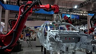FILE - Visitors look at the robotic arms assembly a vehicle frame during the annual World Robot Conference at the Etrong International Exhibition and Convention Center in the 