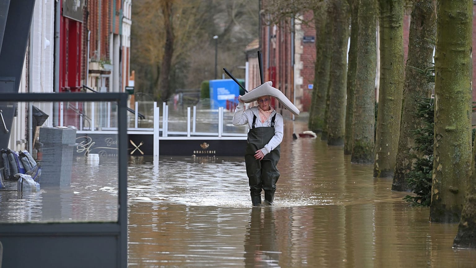 A woman carries a chair on her head as she walks in a flooded street of Arques, northern France, 4 January 2024. 