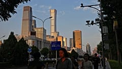 An evening sunlight casts on a woman as people walk near the Central Business District during the rush hour in Beijing on Monday, Aug. 14, 2023.