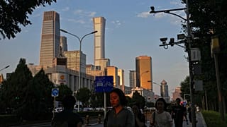 An evening sunlight casts on a woman as people walk near the Central Business District during the rush hour in Beijing on Monday, Aug. 14, 2023.