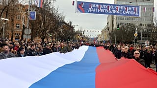 Bosnian Serbs march carrying a giant Serbian flag during a ceremony on the occasion of "the day of Republika Srpska" in the Bosnian town of Banja Luka in 2022.