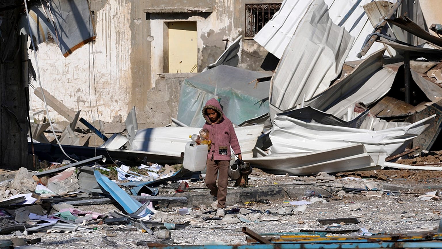 طفل فلسطيني يسير بجوار مصانع دمرت في القصف الإسرائيلي لقطاع غزة في دير البلح- 13 يناير، 2024.