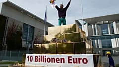 Egy tüntető kiabál egy hamis aranypiramis tetejéről a vagyon újraelosztásáért tartott tüntetésen a berlini kancellária előtt 2012. szeptember 25-én