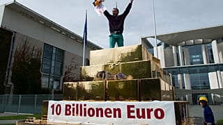 Egy tüntető kiabál egy hamis aranypiramis tetejéről a vagyon újraelosztásáért tartott tüntetésen a berlini kancellária előtt 2012. szeptember 25-én