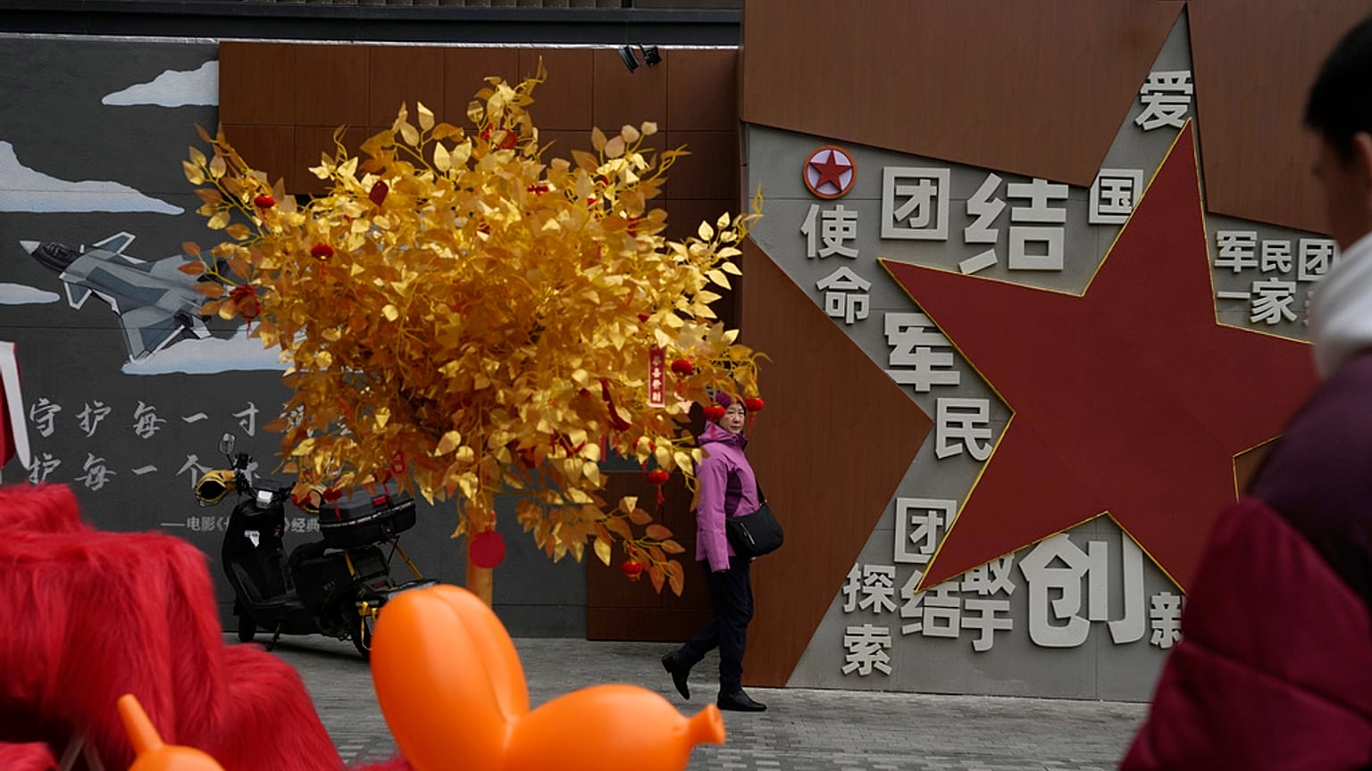 A women walks past a display depicting a golden tree and government propaganda calling for patriotism and unity between society and military at a mall in Beijing, Wednesday, J