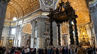 Visitors walk by the 17th century, 95ft-tall bronze canopy by Giovan Lorenzo Bernini surmounting the papal Altar of the Confession in St. Peter's Basilica
