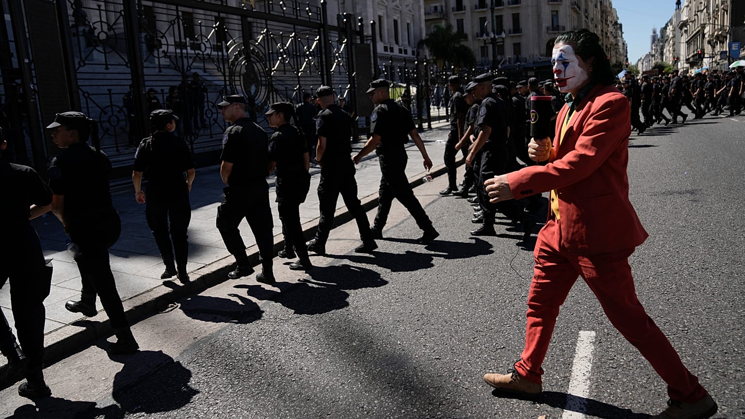 A protester in a Joker costume walks behind police leaving the area near Congress at the end of a protest during a national strike in Buenos Aires, 