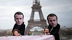Aktivisten, die Masken von Emmanuel Macron tragen, legen ihre Hände über geknebelte Frauen während einer Demonstration in Paris, 24. November 2023