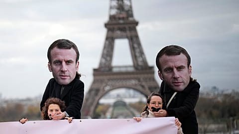 Emmanuel Macron maszkját viselő aktivisták kezüket a betömött szájú nőkre helyezik egy párizsi tüntetésen, 2023. november 24-én.
