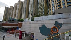 Bir adam 15 Eylül 2021'de Pekin'deki Evergrande şehir plazasında Evergrande geliştirme projelerini ve arkasındaki apartman binalarını gösteren bir Çin haritasının yanında yürüyor.