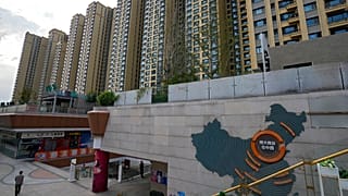 A man walks by a China's map showing Evergrande development projects and its apartment buildings are seen behind, at an Evergrande city plaza in Beijing, 15 Sept. 2021.