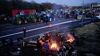 Farmers warm themselves around a bonfire as they block a highway with their tractors in Ourdy, south of Paris, Wednesday, Jan. 31.