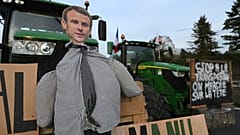 Ein Bildnis des französischen Präsidenten Emmanuel Macron ist auf einem Traktor zu sehen, während Landwirte auf einer Landstraße demonstrieren.