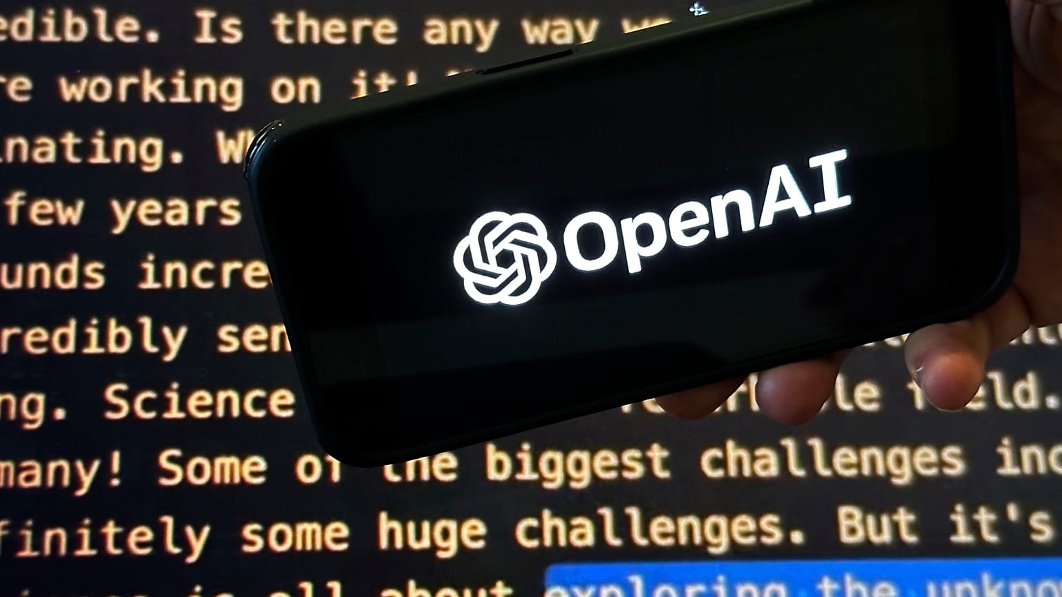 Логотип OpenAI появляется на мобильном телефоне перед экраном, на котором отображается часть сайта компании.