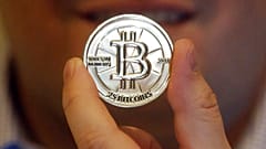  На этом фото 3 апреля 2013 года мужчина держит токен с символом криптовалюты в своем магазине в Сэнди, штат Юта. 