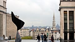 Menschen mit Gepäck vor der Kulisse der Stadt Brüssel.