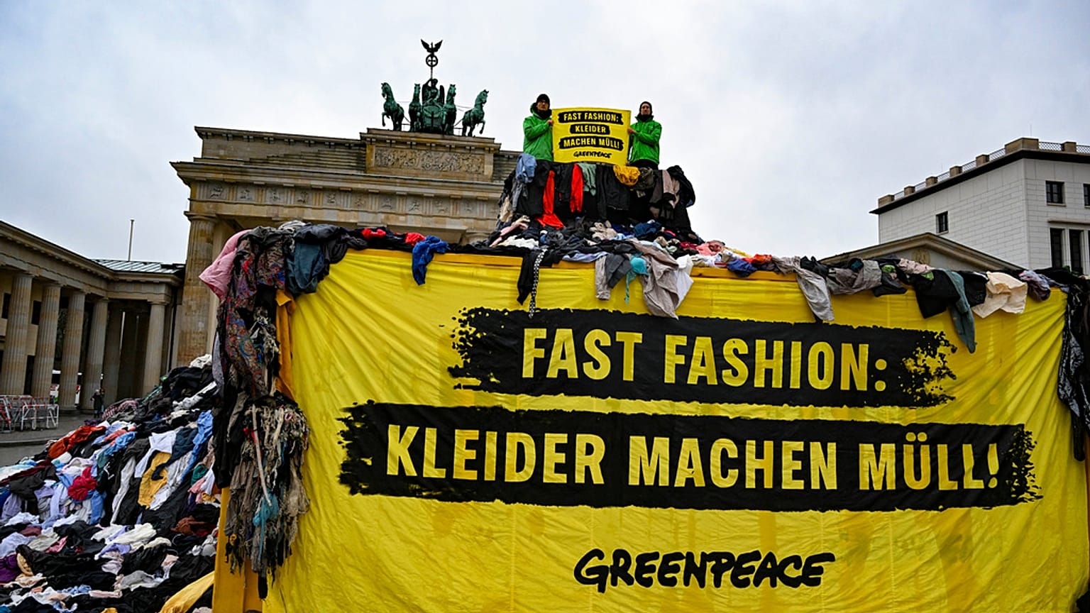 "Fast fashion: as roupas fazem lixo!" é escrito num cartaz exibido por activistas do Greenpeace em frente à Porta de Brandemburgo, em Berlim