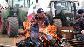 A farmer sits next to a fire during a gathering near the highway junction in Melegnano, near Milan, Italy, Wednesday, 7 February, 2024.