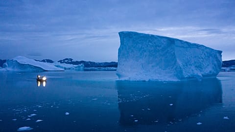  A boat navigates at night next to large icebergs in eastern Greenland. 
