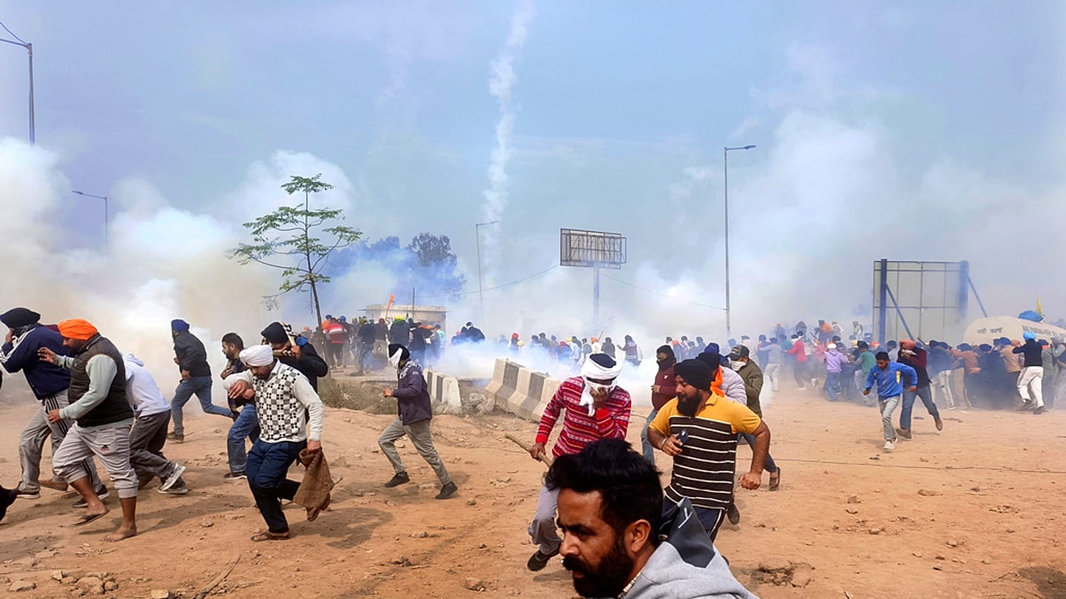 Farmers run for cover after police fired tear gas to disperse protesting farmers who were marching to New Delhi near the Punjab-Haryana border at Shambhu, India, Tuesday, Feb.