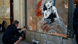 A jogger stops to take photos on his phone of a new artwork by British artist Banksy opposite the French Embassy, in London, 2016.