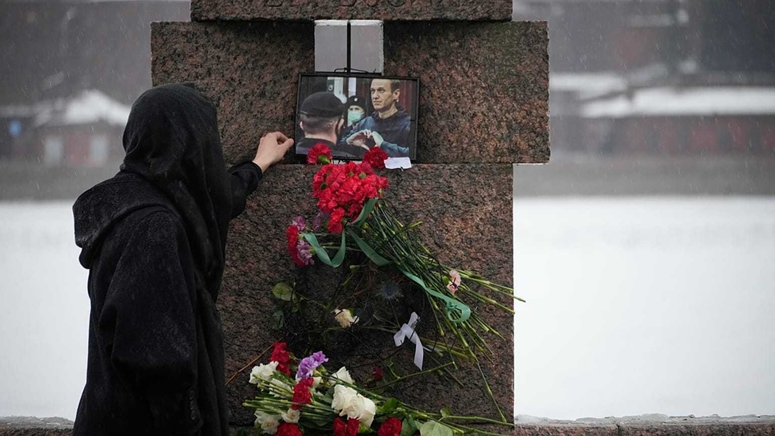 Una mujer toca una foto de Alexéi Navalni tras depositar flores para rendirle un último homenaje en el Monumento a las Víctimas de la Represión Política en San Petersburgo.