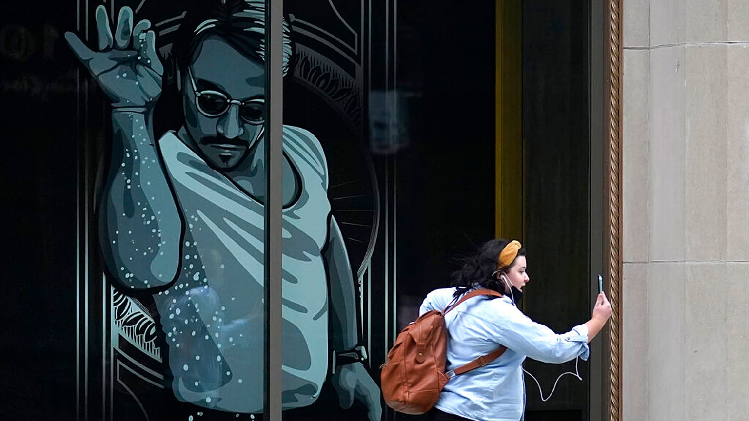 A passer-by uses a mobile device near a window featuring a likeness of chef and social media star Salt Bae outside the Nusr-Et Boston restaurant, Sept. 29, 2020.