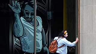 A passer-by uses a mobile device near a window featuring a likeness of chef and social media star Salt Bae outside the Nusr-Et Boston restaurant, Sept. 29, 2020.