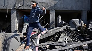 شاب فلسطيني يمشي فوق أنقاض منزل عائلة في دير البلح دمره القصف الإسرائيلي على غزة