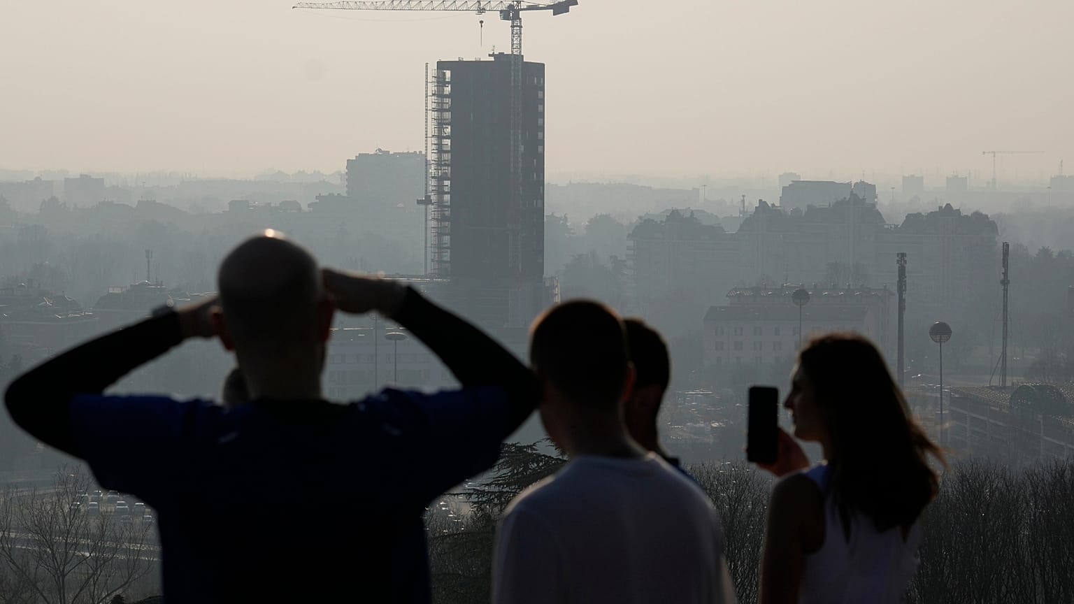 Des athlètes font une pause alors qu'ils courent sur la colline de San Siro et regardent l'horizon de Milan, Italie, mardi 20 février 2024.