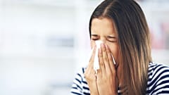 A person suffering from allergies blows their nose.