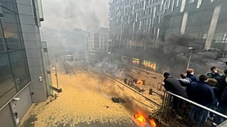 La gente mira por un balcón mientras arden incendios y se esparce heno en la calle durante una protesta de agricultores en Bruselas, el 26 de febrero, 2024.