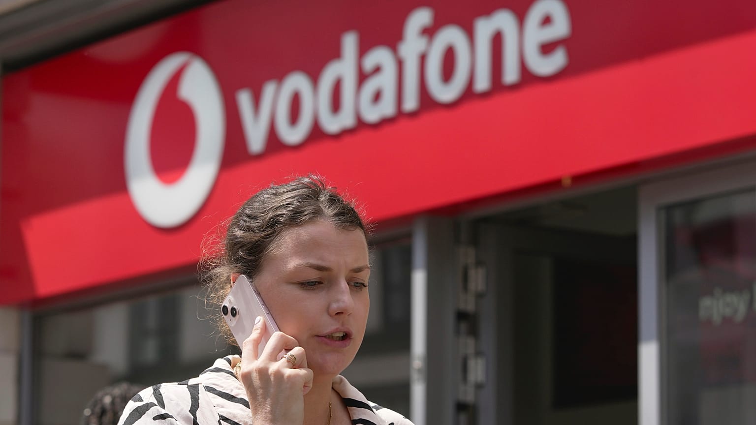 A woman talking on her mobile walks past a Vodafone store in London. June 14, 2023. 