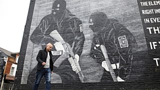 Loyalist activist Jamie Bryson walks past a Ulster Volunteer Force mural in east Belfast, Northern Ireland, Tuesday, Oct. 15, 2019. 
