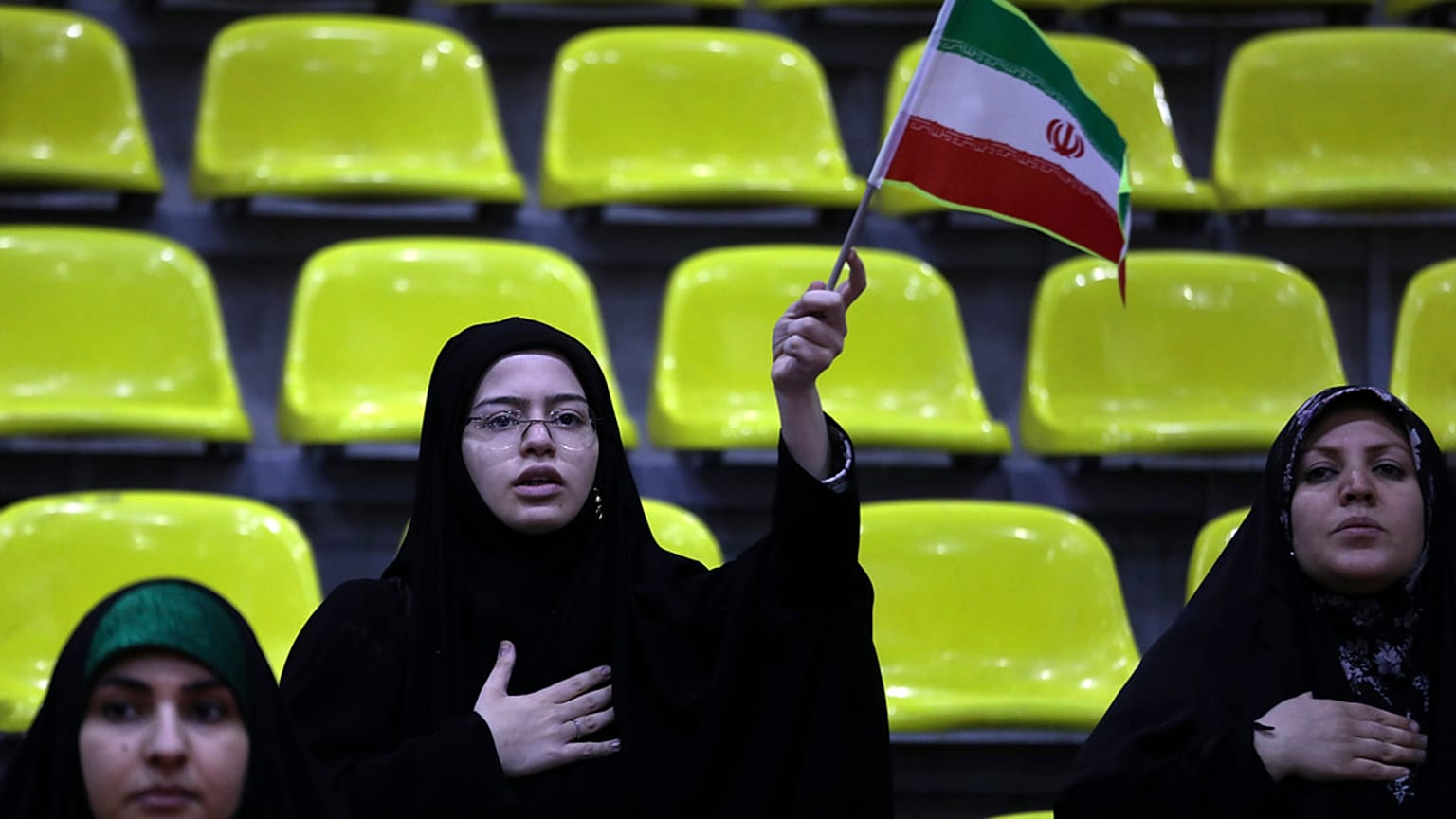 Iranian women listen to their country's national anthem as one of them waves the national flag during an election campaign rally ahead of the March 1, parliamentary and Assemb
