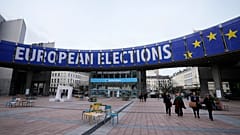 Des personnes marchent sous une bannière annonçant les élections européennes devant le Parlement européen à Bruxelles.