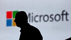 In this Nov. 7, 2017, file photo, an unidentified man is silhouetted as he walks in front of Microsoft logo at an event in New Delhi, India.