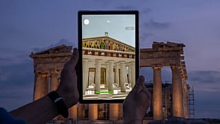 A man holds up a tablet showing a digitally overlayed virtual reconstruction of the ancient Parthenon temple, at the Acropolis Hill in Athens, Greece on Tuesday, June 13, 2023