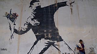 عامل فلسطيني يستريح تحت جدارية رسمها الفنان البريطاني المجهول بانكسي في محطة وقود، مدينة بيت لحم بالضفة الغربية، 4 أغسطس 2022.