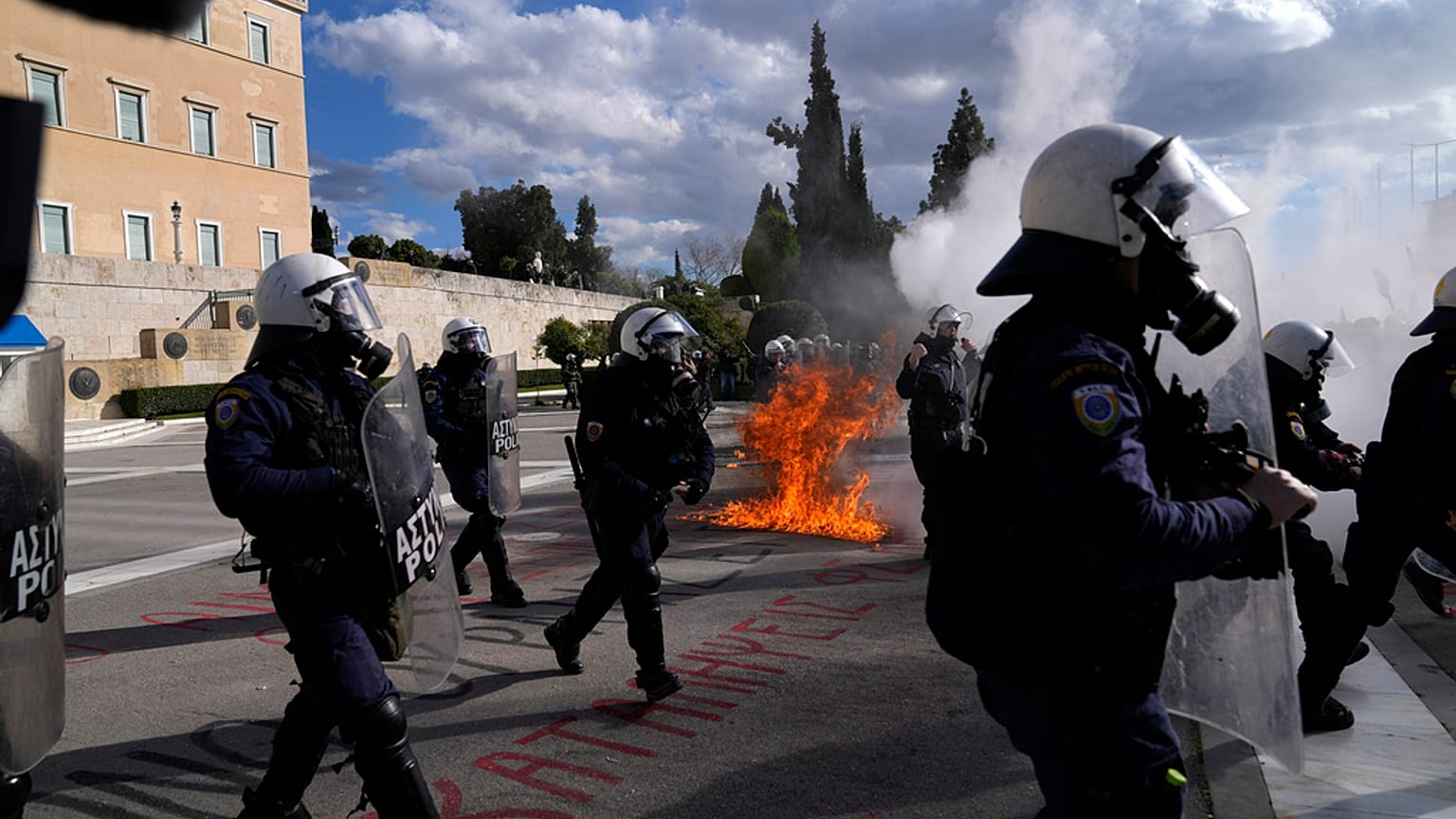 Unruhestifter stehen vor dem Parlament, während im Hintergrund das Feuer eines Molotowcocktails während einer Studentendemonstration in Athen, Griechenland, zu sehen ist, 8. März 2024