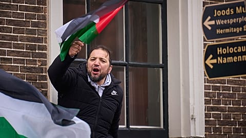 A man waves a Palestinian flag next to signs for the Holocaust Monument and the Jewish Museum as demonstrators protested against Israel's President Isaac Herzog.