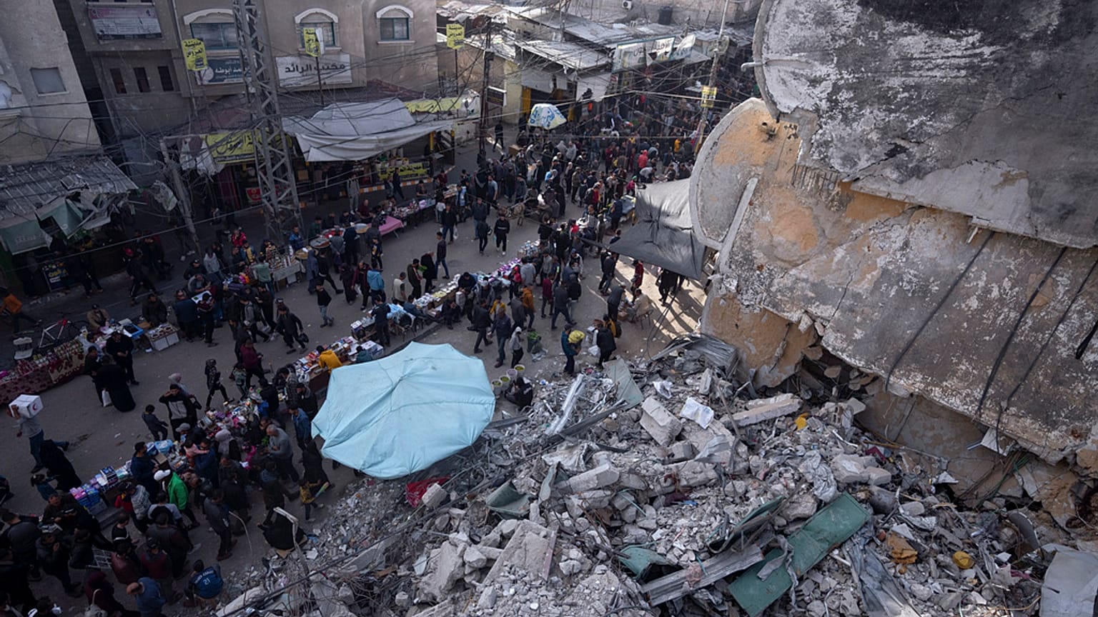 Palestinians shop at a local market next to a destroyed residential building by the Israeli airstrikes, during the Muslim holy month of Ramadan, in Rafah, Gaza Strip, Thursday