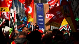 People listen to speeches near the European Commission headquarters, background, during a protest by European trade unions in Brussels, Friday, April 26, 2019.