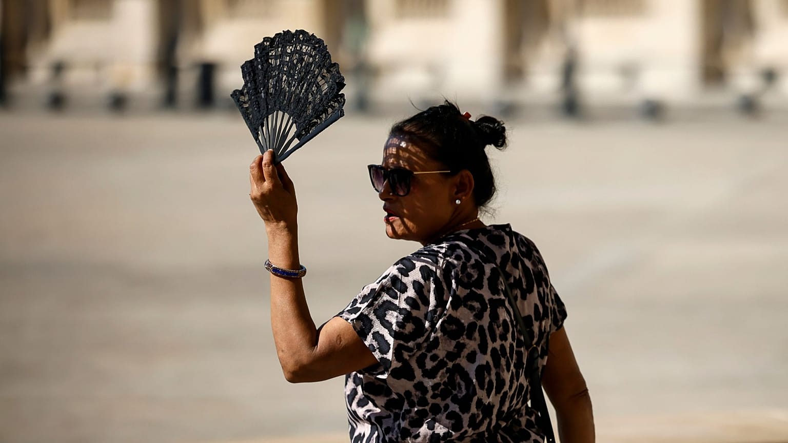 A woman uses a fan in the courtyard of the Louvre museum, September 2023, in Paris.