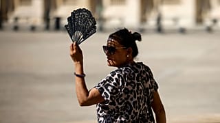 A woman uses a fan in the courtyard of the Louvre museum, September 2023, in Paris.
