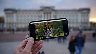 A person watches an announcement on a smart phone outside Buckingham Palace by Kate, the Princess of Wales, Friday, March 22, 2024.