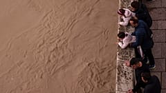 Un grupo de gente observa el río Guadalquivir tras las recientes lluvias bajo el puente romano en Córdoba, España